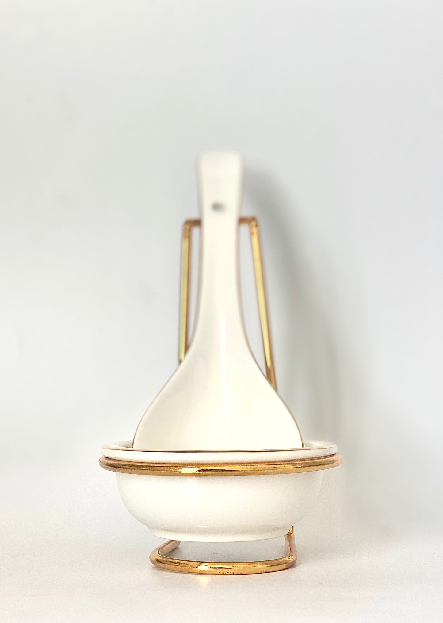 A white oblong shaped ceramic bowl and spoon with a gold stand .