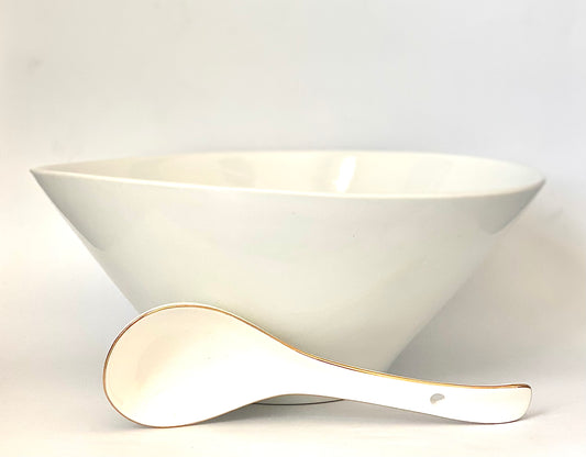 A white oblong shaped ceramic bowl and spoon with a gold stand .