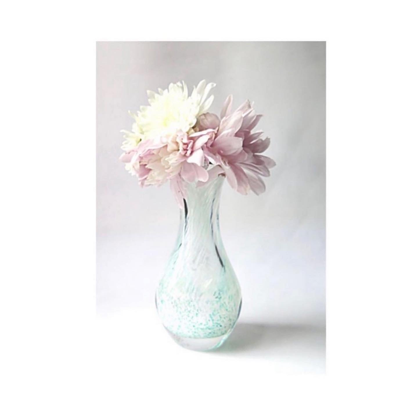 A Caithness glass bud vase in speckled sea green with a soft creamy swirl.